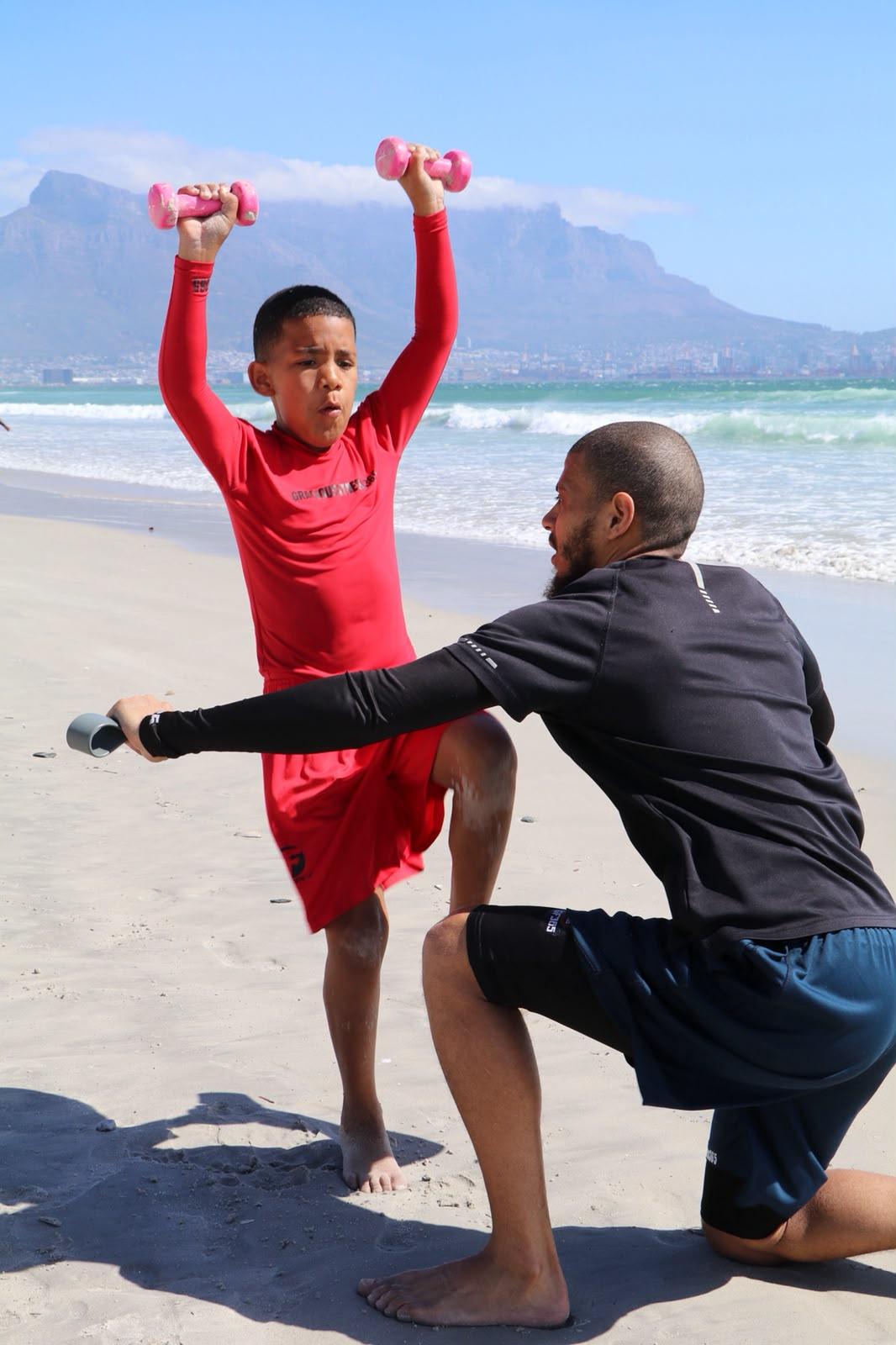 Overhead dumbbell press, coached on the beach